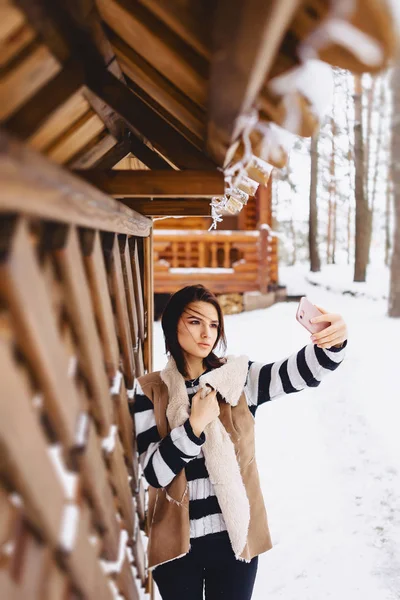 Jovem com telefone em colete em contra de casa de campo de madeira — Fotografia de Stock