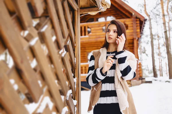 Jeune fille avec téléphone en gilet sur contre de chalet en bois — Photo
