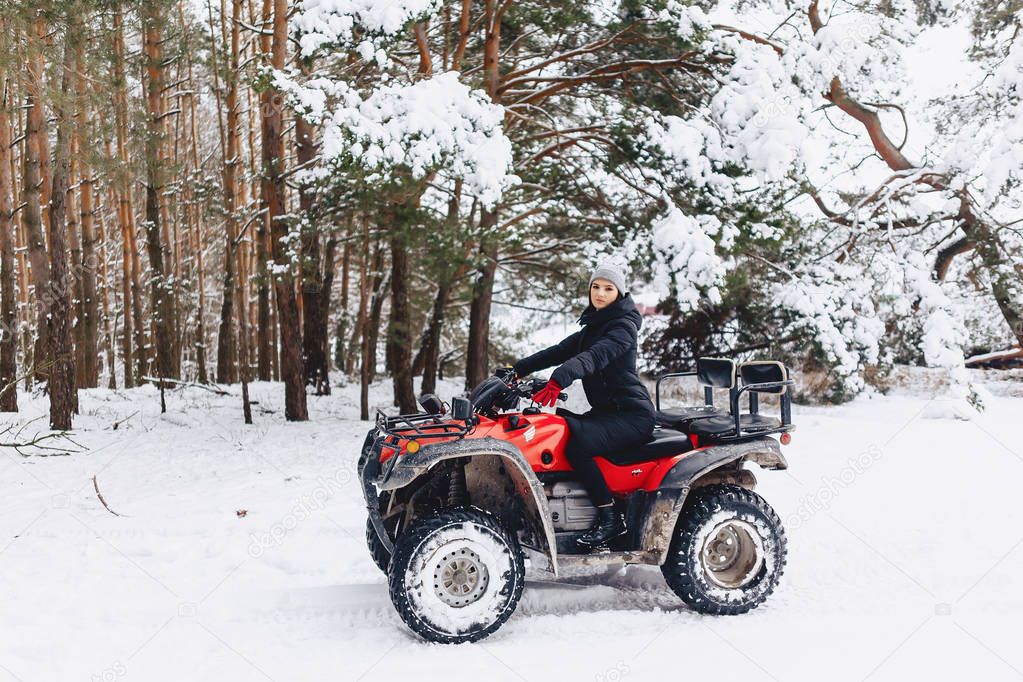 young girl on a motorcycle rides in snow-covered pine forest in 