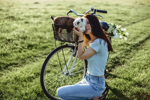 La chica camina con un cachorro en un campo en una bicicleta en la parte posterior — Foto de Stock