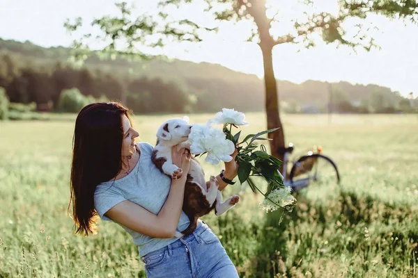 La chica camina con un cachorro en un campo en una bicicleta en la parte posterior — Foto de Stock