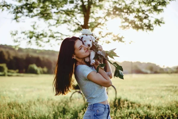 La chica camina con un cachorro en un campo en una bicicleta en la parte posterior — Foto de Stock