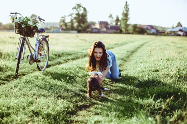 La chica camina con un cachorro en un campo en una bicicleta en la parte posterior — Foto de Stock