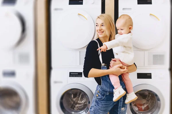 Mor med baby på bakgrunden av tvättmaskiner — Stockfoto