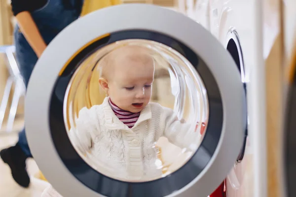 O bebê olha pela janela da máquina de lavar roupa — Fotografia de Stock