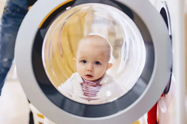O bebê olha pela janela da máquina de lavar roupa — Fotografia de Stock
