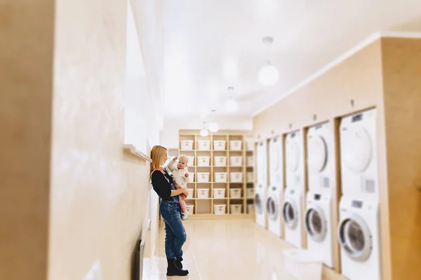 Woman with a child on her hands in the laundry is waiting for cl — Stock Photo, Image