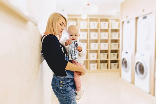 Woman with a child on her hands in the laundry is waiting for cl — Stock Photo, Image
