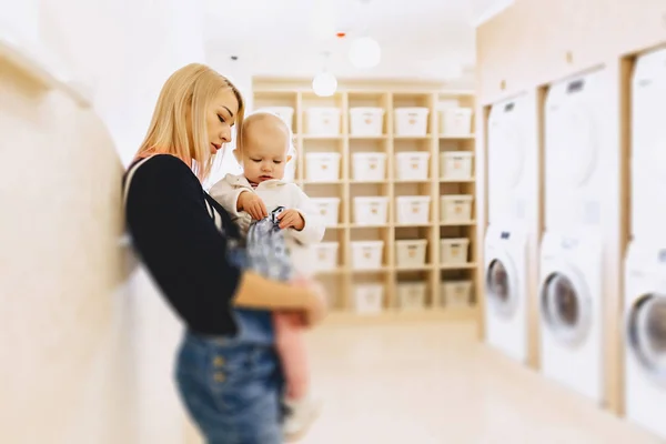 Woman with a child on her hands in the laundry is waiting for cl — Stock Photo, Image