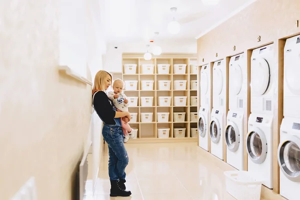 Kvinna med ett barn på hennes händer i tvätten väntar på cl — Stockfoto