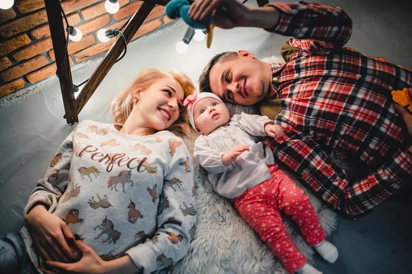 Mom, dad and baby lie on a woolen carpet and smile — Stock Photo, Image