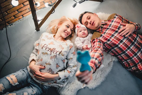 Mom, dad and baby lie on a woolen carpet and smile — Stock Photo, Image