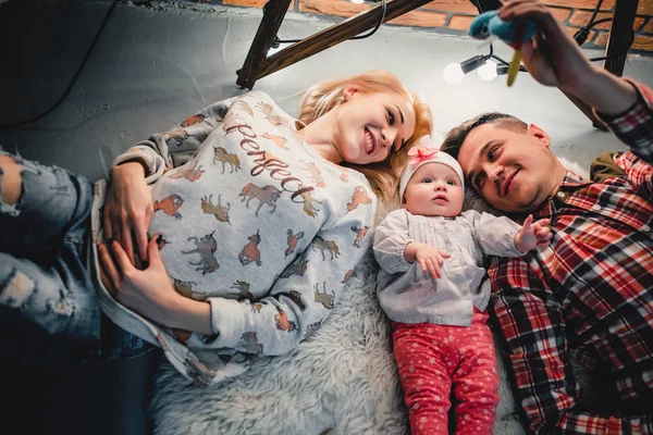 Mom, dad and baby lie on a woolen carpet and smile — Stock Photo, Image