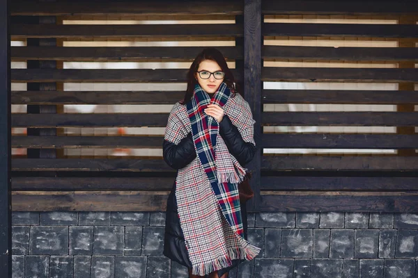 Menina bonita em óculos e um lenço contra uma parede de madeira — Fotografia de Stock