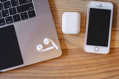 bir dizüstü bilgisayar, telefon ve ahşap bir masa üzerinde bir kablosuz kulaklık