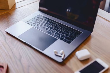 bir dizüstü bilgisayar, telefon ve ahşap bir masa üzerinde bir kablosuz kulaklık