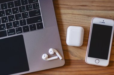 bir dizüstü bilgisayar, telefon ve ahşap bir masa üzerinde bir kablosuz kulaklık