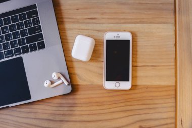 bir dizüstü bilgisayar, telefon ve ahşap bir masa üzerinde bir kablosuz kulaklık