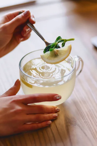 A cup of hot tea with mint and lemon mixes the girl with a spoon — Stock Photo, Image