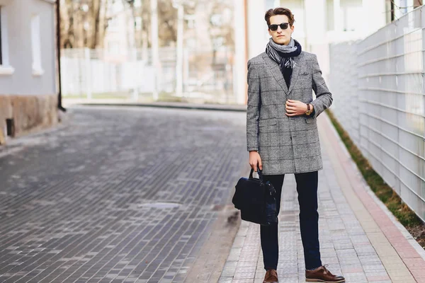 Elegante ragazzo in occhiali da sole in cappotto con valigetta sulla strada — Foto Stock