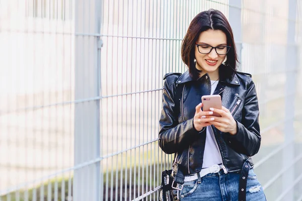 Mujer en chaqueta de cuero en gafas de mensajería en el teléfono y sonrisas — Foto de Stock