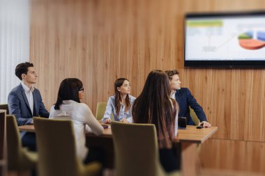 büyük takım insanlar bir masada dizüstü bilgisayarlar için çalışıyor, tabletler ve kağıtlar, arka planda büyük bir TV ahşap duvar seti