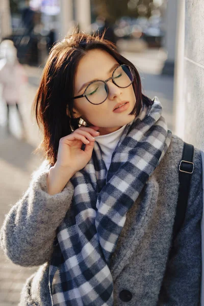 Attractive young girl wearing glasses in a coat walking on a sunny day — Stock Photo, Image