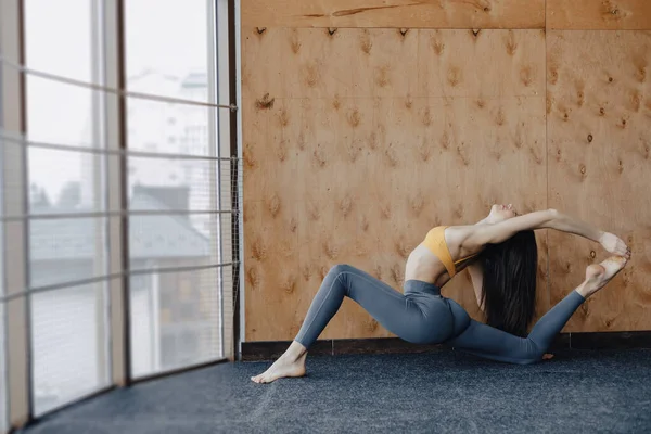 Joven chica atractiva haciendo ejercicios de fitness con yoga en el suelo sobre un fondo de madera — Foto de Stock
