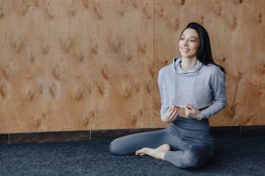 Genç çekici Fitness kız yoga dersleri dinlenme, ahşap bir duvarın arka planda pencerenin yakınında yerde oturuyor