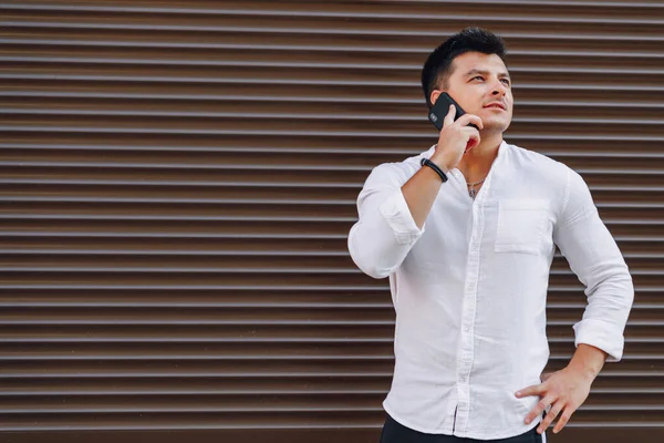 Ung snygg kille i skjorta talar via telefon på enkel bakgrund — Stockfoto