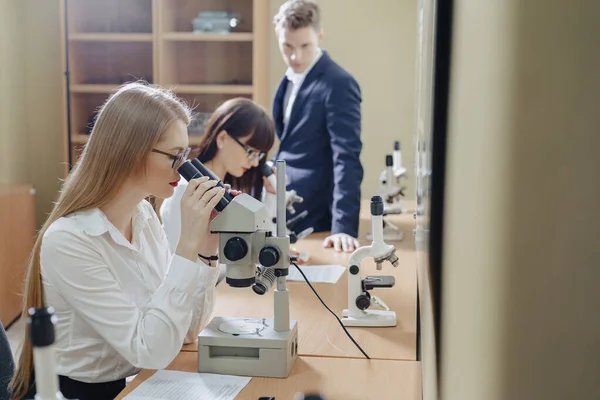 Två flickor och en pojke arbetar med Mikroskop — Stockfoto
