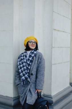 Basit bir ışık arka planda ceket ve sarı Beret gözlüklerini çekici gülümseyen genç kız