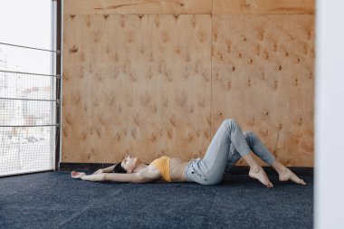 Genç çekici Fitness kız yoga dersleri dinlenme, ahşap bir duvarın arka planda pencerenin yanında yerde yatıyor