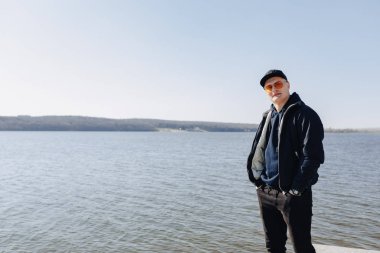 turuncu gözlük, ceket ve kap şık genç çocuk, ilkbahar veya sonbaharda göl etrafında yürümek