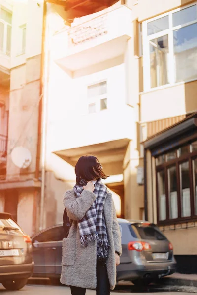 Приваблива позитивна молода дівчина в окулярах на пальто на тлі будівель на машинах — стокове фото
