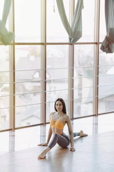 Chica atractiva joven haciendo ejercicios de fitness con yoga en el suelo contra el fondo de ventanas panorámicas — Foto de Stock