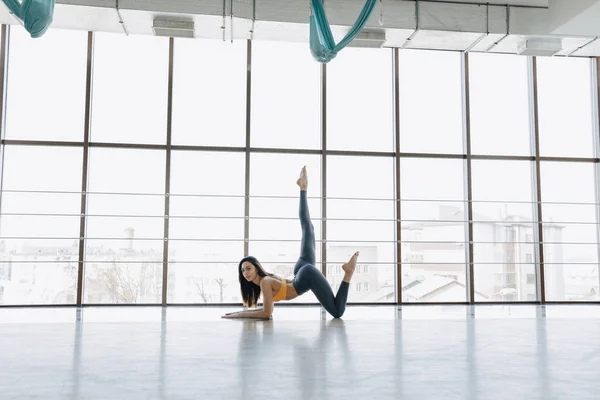 Chica atractiva joven haciendo ejercicios de fitness con yoga en el suelo contra el fondo de ventanas panorámicas — Foto de Stock