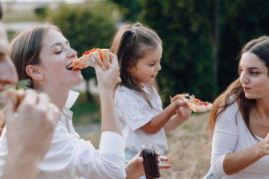 Küçük kız piknikte, pizzada, içkide, yazda ve çimlerde eğleniyor.