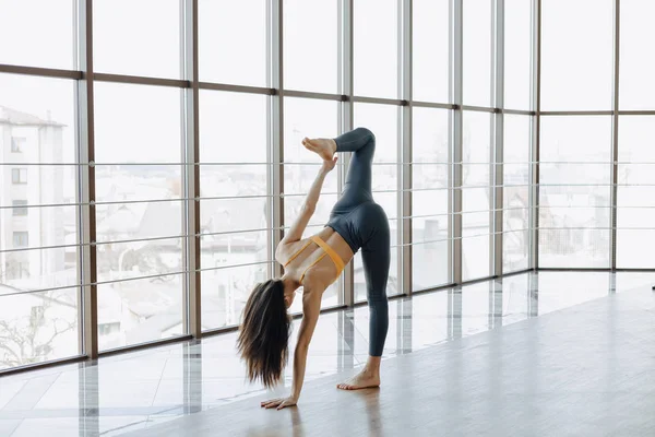 Jeune fille attrayante faisant des exercices de fitness avec yoga sur le sol sur le fond de fenêtres panoramiques — Photo