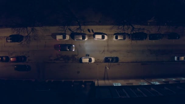 맨 위에서 보면,그 차는 저녁에 좁은 거리에 주차되어 있습니다. 야간 도시. 공중 조사. — 비디오