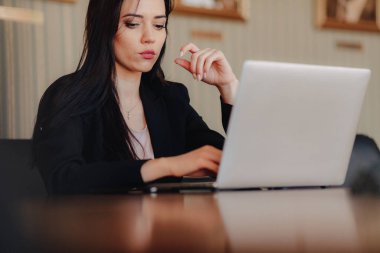 Tek başına ofis veya oditoryumda bir dizüstü bilgisayar ve telefon bir masada oturan iş tarzı giysiler genç çekici duygusal kız