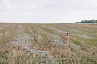 Tarlada saman oynayan küçük sarışın çocuk. Yaz, güneşli hava, çiftçilik. Mutlu çocuk.