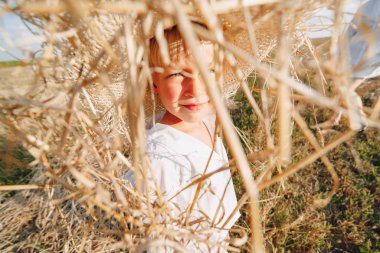 Hasır şapkalı sarışın çocuk biçilmiş samanlıkta oynuyor. Yaz, güneşli hava, çiftçilik. Mutlu çocukluk. güneşli.