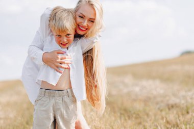 Sarışın küçük çocuk samanlı, beyaz saçlı annesiyle oynuyor. Yaz, güneşli hava, çiftçilik. Mutlu çocukluk. aile.