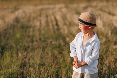 Hasır şapkalı sarışın çocuk biçilmiş samanlıkta oynuyor. Yaz, güneşli hava, çiftçilik. Mutlu çocukluk. güneşli.