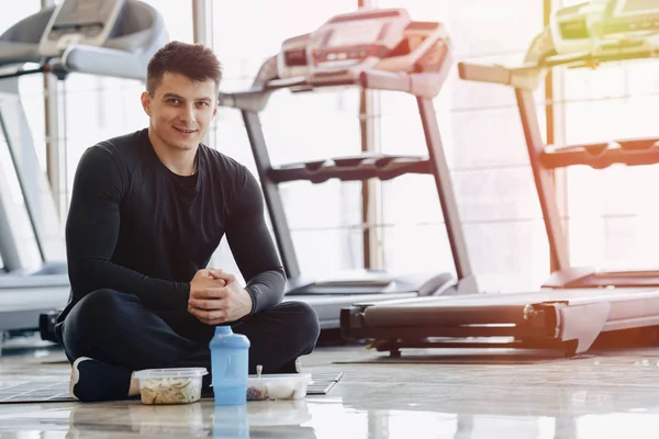 Spor salonunda şık bir adam yerde dinleniyor ve sağlıklı yiyecekler yiyor. Sağlıklı Yaşam Tarzı.