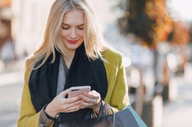 Güneşli bir havada sokakta paketleri olan sevimli, mutlu, çekici, sarışın bir kadın. Alışverişten sonra telefonla konuşuyor, olumlu duygular..