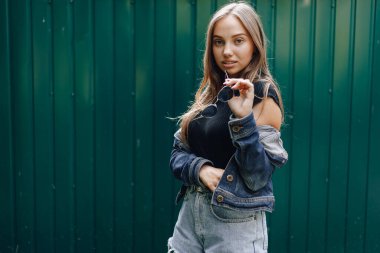 Kot elbiseli, gözlüklü, koyu yeşil arka planda mesaj atmak için boş bir yeri olan oldukça çekici bir genç kız..