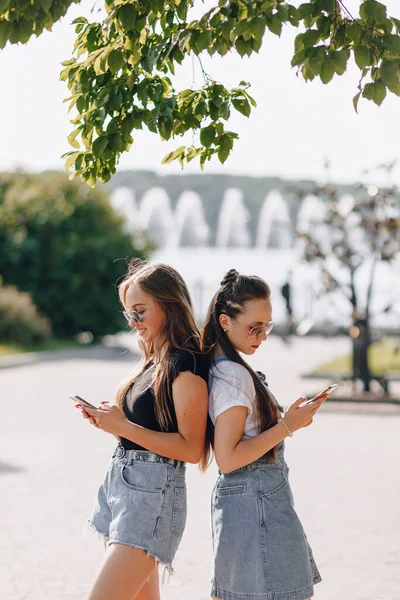 Duas Meninas Bonitas Passeio Parque Com Telefones Dia Ensolarado Quente — Fotografia de Stock