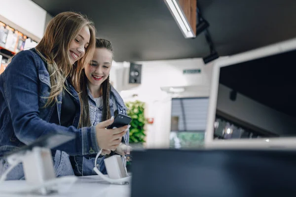 young attractive girls in electronics shop testing phones on a shop window. phone store. concept of buying gadgets.